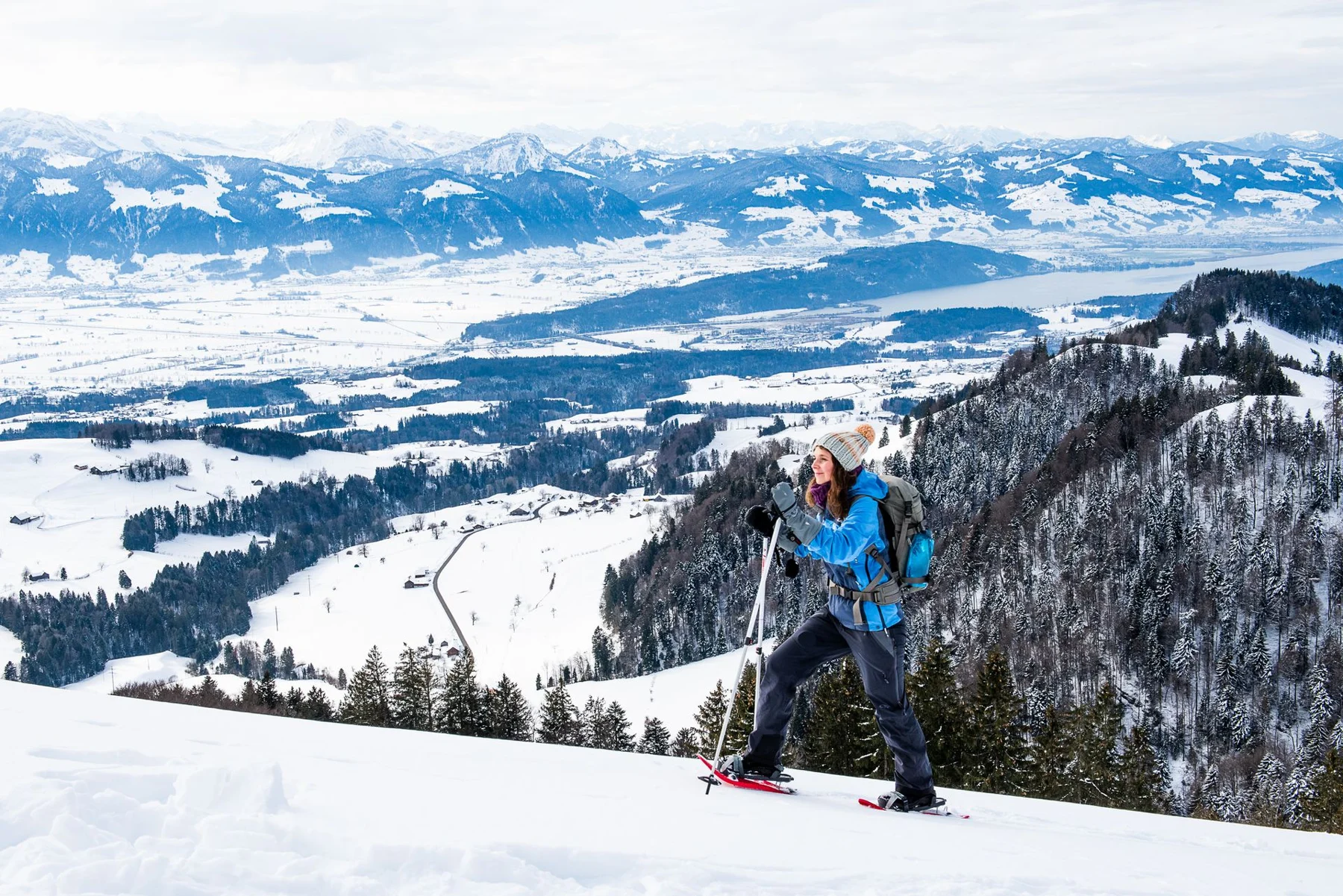 Schneeschuhwanderin im Atzmännig mit Blick über die verschneite Landschaft, den See und die Berge