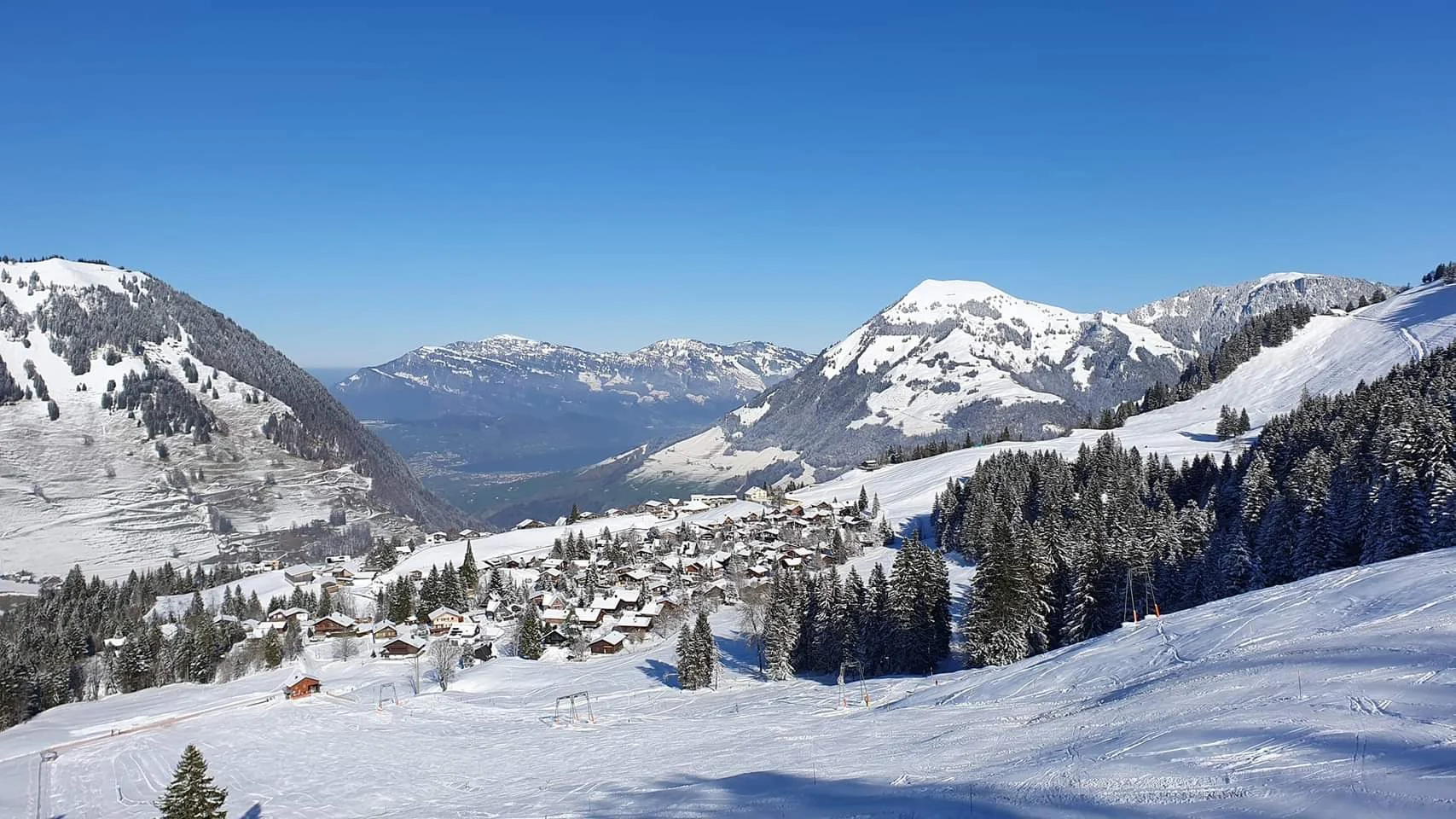 Verschneites Wirzweli mit Chalets, Tannen und Bergpanorama unter blauem Himmel